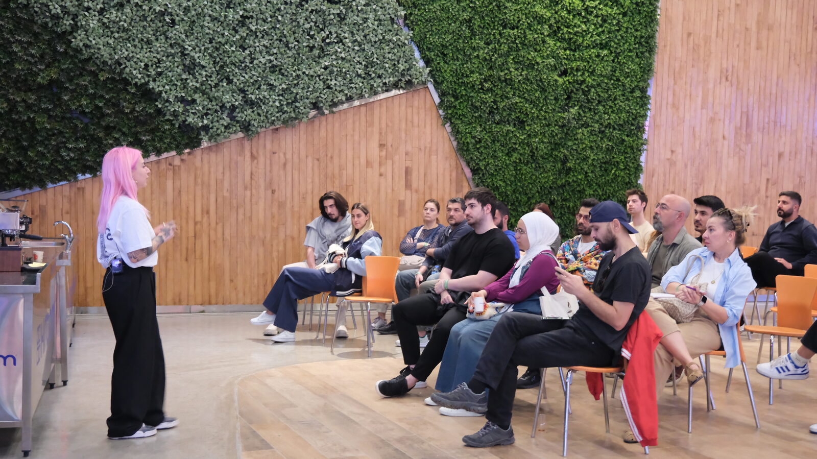 People seated in a courtyard with a green hedge wall behind them