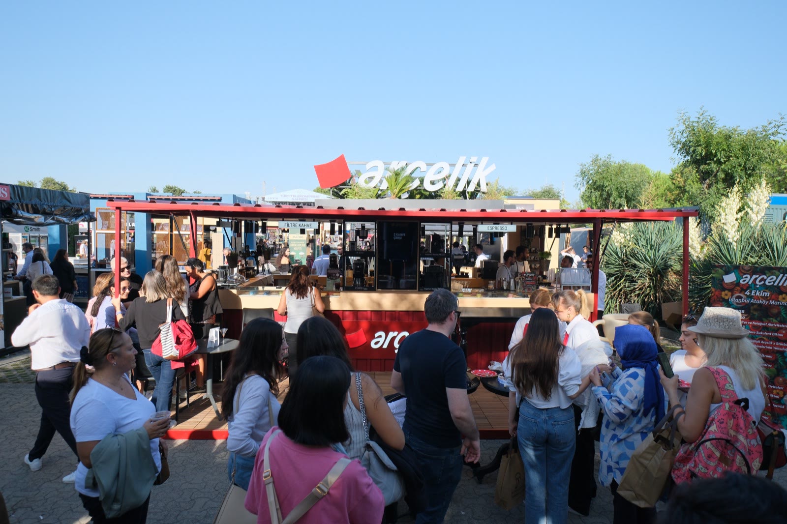 Visitors queuing at a red brand stand on a sunny afternoon